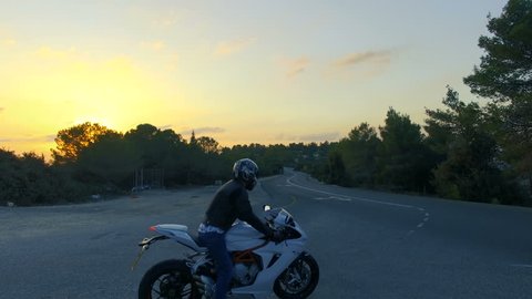 Aerial shot of a motorcycle rider driving away on a road during sunset