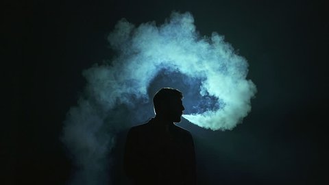 The man exhale electronic cigarette smoke on the dark background. Real time capture