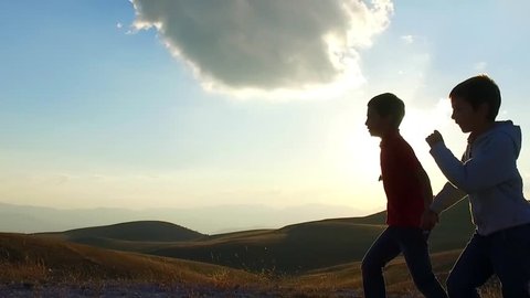 SLOW MOTION: Kid brothers silouette running in the mountains of Campo Imperatore, Italy, at the sunset. 
