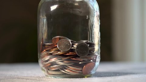 A close up shot of a half full jar as coin money is dropped into it until it is full.