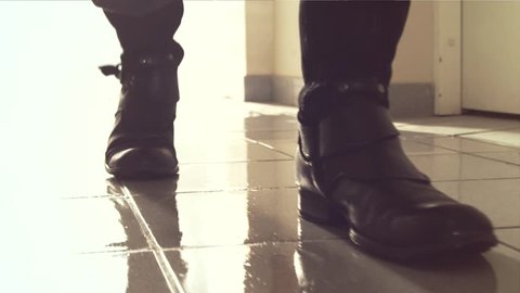 Heavy footsteps along the corridor. The old boots in slow motion. Back light and reflection in wet floor. Steps unknown male feet. Boots closeup. Shooting with dolly.