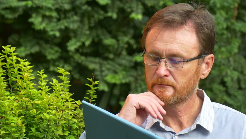 a Tall Red-Haired Man Reads an Electronic Book. he Sits Some Time on a Bench, Finishing Reading of a Last Paragraph. After That the Man Rises From the Bench and Leaves Away.