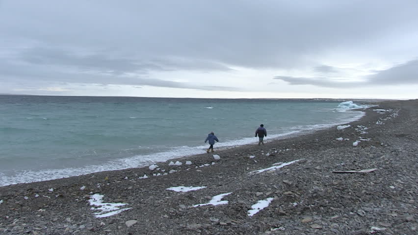 Inuit man and girl walk along an icy coast. 