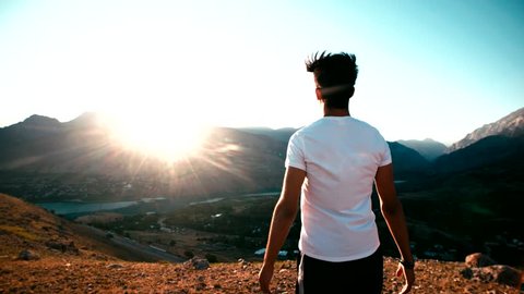 young Asian male reaching to the top of the mountain area, standing on top of the mountain, raised hands, slow motion