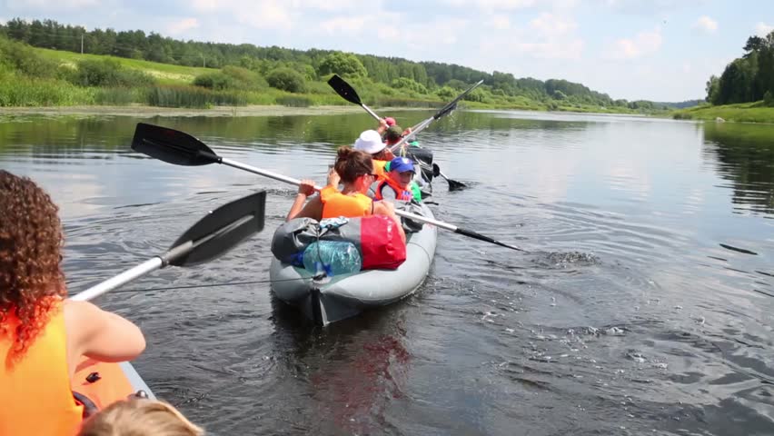 Back of people rowing and boy in three canoe concatenated with rope on river Tvertsa at summer day.