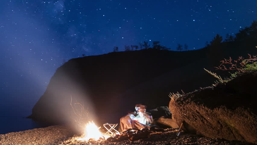Moving stars above camping at night. Man and woman enjoy campfire amd view of milky way on the sky. Camera moving on slider. Time lapse
