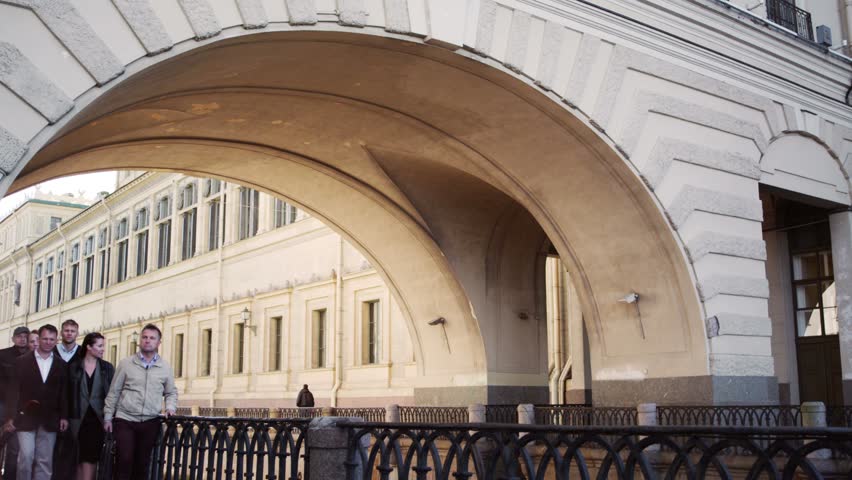 Tourist group with guide come close to the camera and look at the object behind. Background of old building with arch