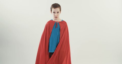 Boy with a superhero cape pretends to fly on a white studio background