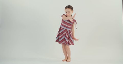 Little girl wearing a dress dances on a white studio background