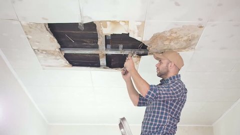 young man makes an emergency inspection of ceiling and use Tablet PC. public utilities. Ceiling panels damaged huge hole in roof from rainwater leakage.Water damaged ceiling , Insurance agent.