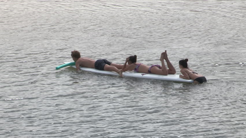 Three teenagers relaxing on long board in the river