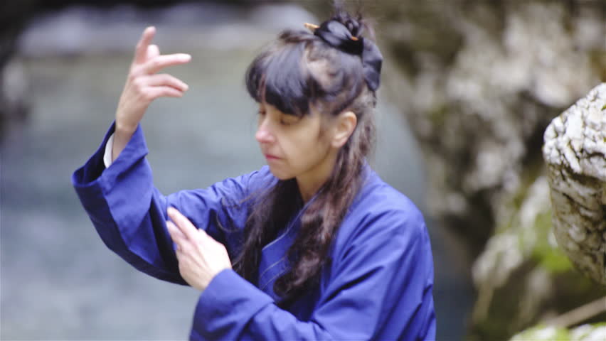 Woman in blue kimono stretch hands around making form exercise 4K. Close up tracking person in shallow focus training martial arts. River in background out of focus.