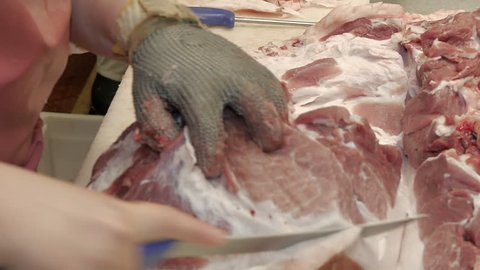 Closeup of the hands of a butcher cutting slices of raw meat off a large loin