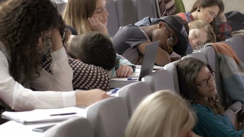 A lot of tired young people sleeping in the lecture hall during a boring presentation. Unmotivated young students feeling exhausted in the auditorium during a presentation.