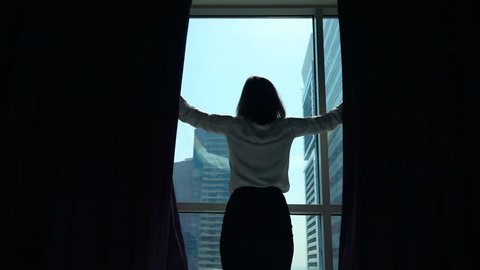 Young businesswoman unveil curtain and looking out of window in the office super slow motion
