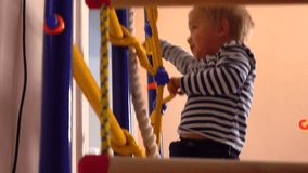 Happy little blond boy climbs up the ladder in playroom. Kid sport, success or achievement concepts. 4K video