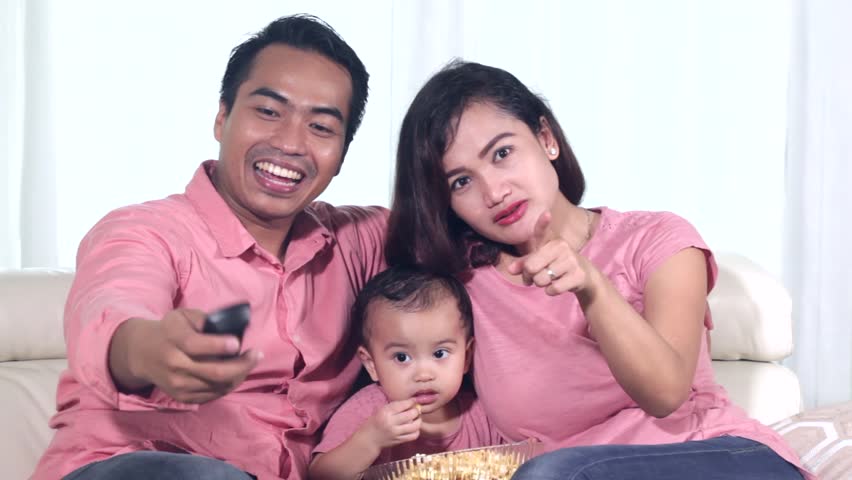 Happy Asian family sitting on the sofa while watching television and eating popcorn at home