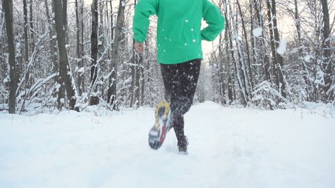 Slow Motion Young Sportsman Running Through Snowy Forest. Training and exercising outdoors when cross country running in inspirational winter landscape. Sports Motivation. 