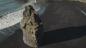 Slow motion drone footage of long basalt sea stack at Reynisfjara beach in Iceland
