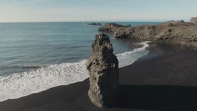 Drone footage of beautiful Reynisfjara beach with long basalt sea stack on sunny day
