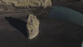 Rotating drone footage of beautiful long basalt sea stack at black sand beach
