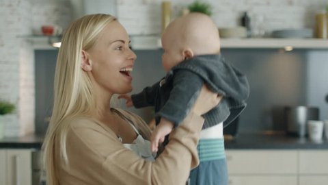 Young Mother Holds and Plays with Her Baby while Standing on the Kitchen. Shot on RED Cinema Camera in 4K (UHD).
