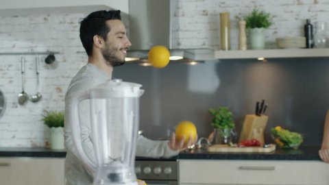 Lively Young Man Impresses His Girlfriend by Juggling Oranges on the Kitchen. Shot on RED Cinema Camera in 4K (UHD).