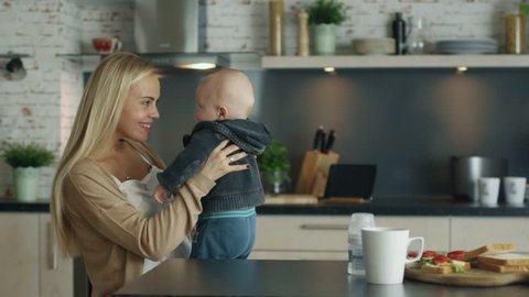 Young Mother Plays with Her Beautiful Baby while Standing on the Kitchen. In Slow Motion. Shot on RED Cinema Camera in 4K (UHD).