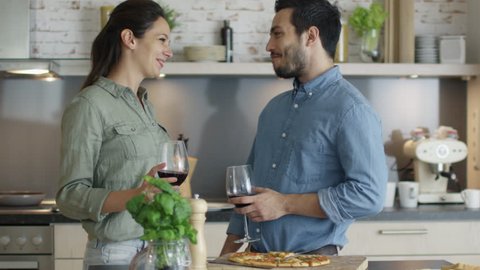 Happy Couple Shares Pizza Slices and Drinks Wine in their Kitchen. Shot on RED Cinema Camera in 4K (UHD).