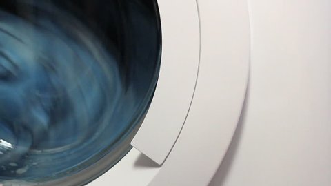 Front view and portion of the porthole of the washing machine during washing and rotation of the drum containing clothes blue