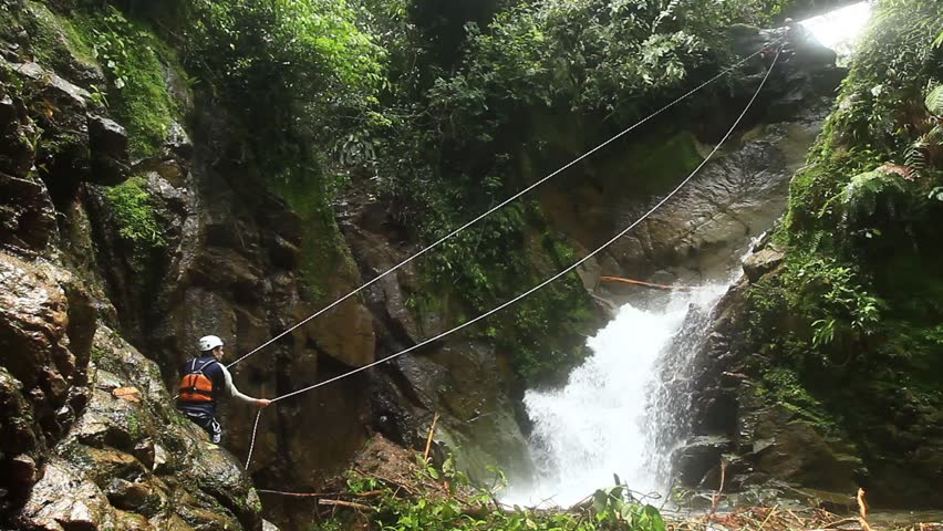 footage of a pesrson crossing a waterfall on a zipline. locked down, wide angle