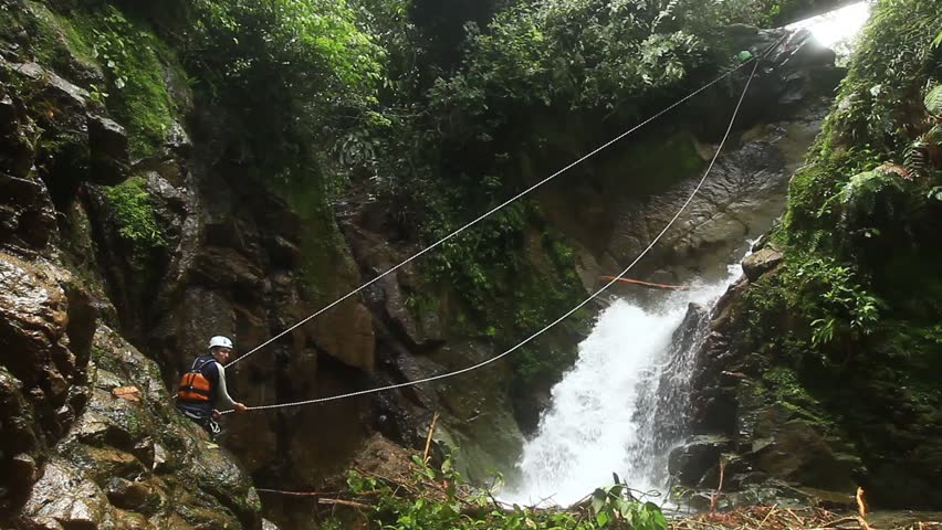 footage of a pesrson crossing a waterfall on a zipline. locked down, wide angle
