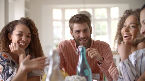 Panning shot of young adult friends talking at dining table