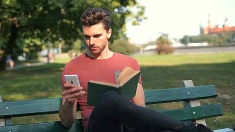 Man receives message on smartphone while reading book in the park
