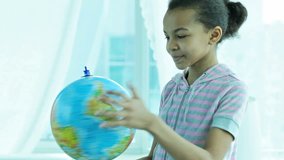 Cute African-American girl spinning the globe and smiling at camera