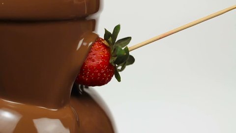 Chocolate fondue fountain with strawberry dipping in on skewer. Slow motion.