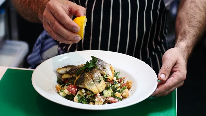 Male chef  squeezing lemon on seabass fish while rotating the plate