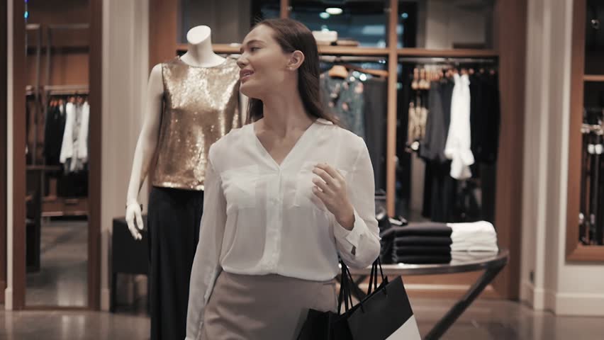 Woman coming out of the clothes store with bags. Girl go from entrance of luxury shop in mall.