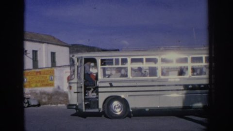 SPAIN 1966: a bus parked on the side of the street, followed by woman at the door of a shop