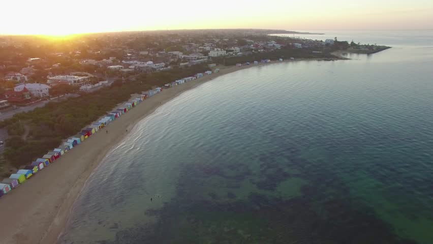 Slow descend over Port Phillip Bay waters facing the sunrise and Brighton Beach bathing huts. Melbourne, Victoria, Australia