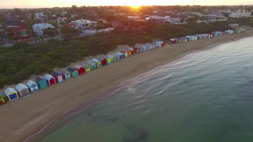 Flying away from Brighton Beach bathing boxes rising high above Port Phillip bay waters at sunrise. Melbourne, Victoria, Australia