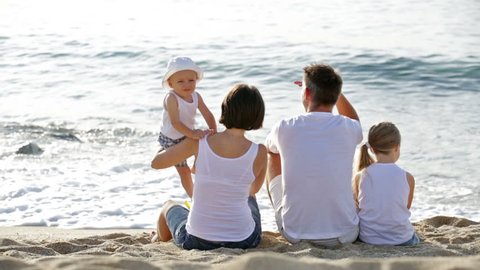   family of four sitting together and looking at sea on beach on summer vacation