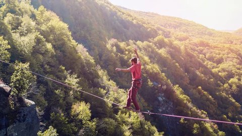 Drone Footage Of Man Balancing On Tightrope Above Mountains Walking Extreme Sport Danger Leisure Adventure Brave Slacklining Fear Sunny