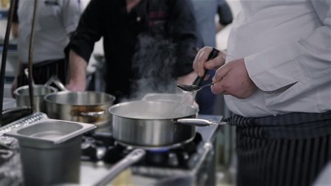 Chef's Masterclass. Chef Stirs Boiling Souce In a Pan In a Commercial Kitchen