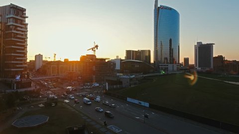 City Sunset over Milan, aerial footage, amazing flight over new Porta Nuova financial district and Porta Garibaldi train station with a road intersection with cars