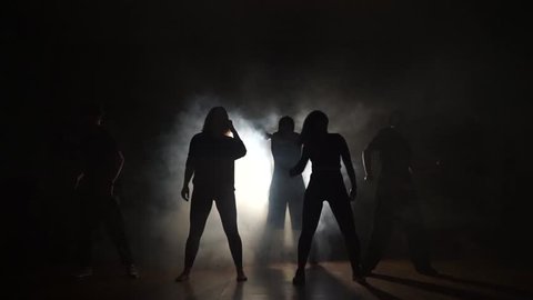 Five dancers are dancing in the smoke in the dark.