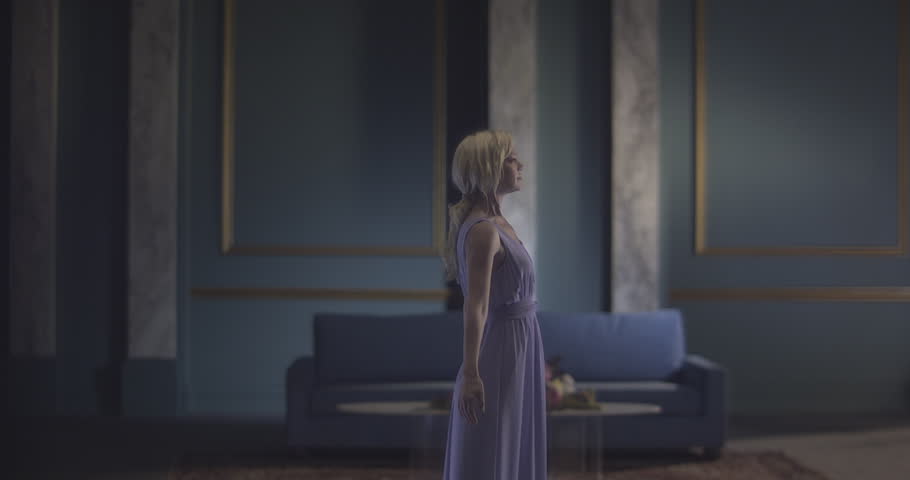 Blue paint splatters all over an woman in an elegant dress, standing in the middle of an old fashioned mansion.