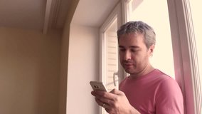 Handsome man in pink tshirt scrolling app in his smartphone. 4K close up steadicam video