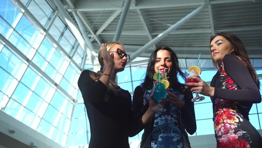 beautiful women are dancing and shaking bodies with cocktails in their hands and clinking glasses. They are communicating and have fun, smiling, playing with hair and catch a sunlight.