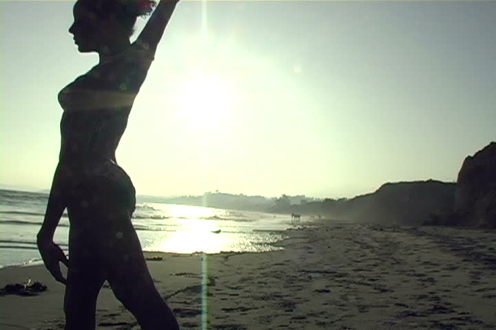 A beautiful, silhouetted young woman performs on the beach.   